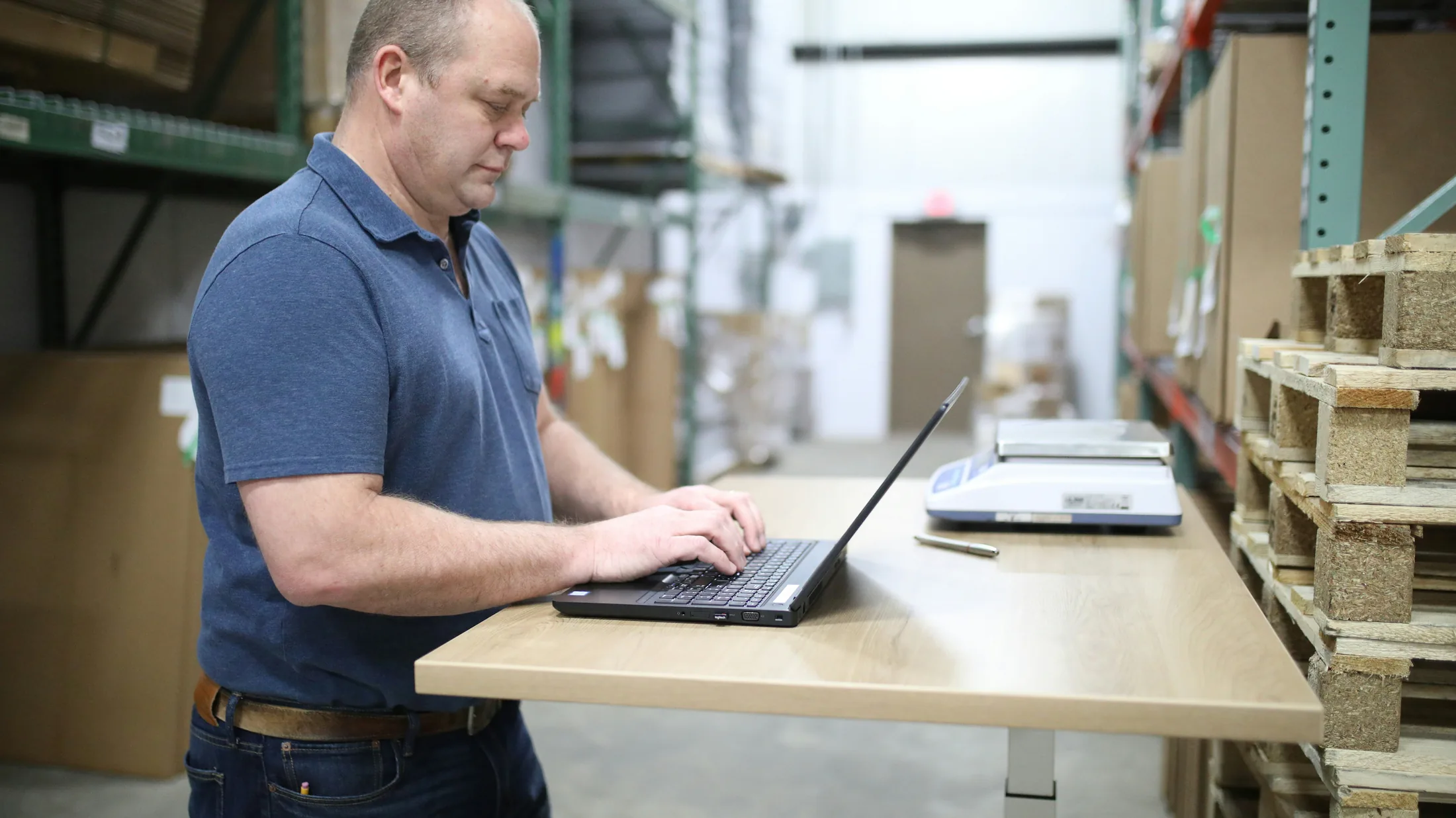 A warehouse operator checking inventory on a laptop beside storage racks